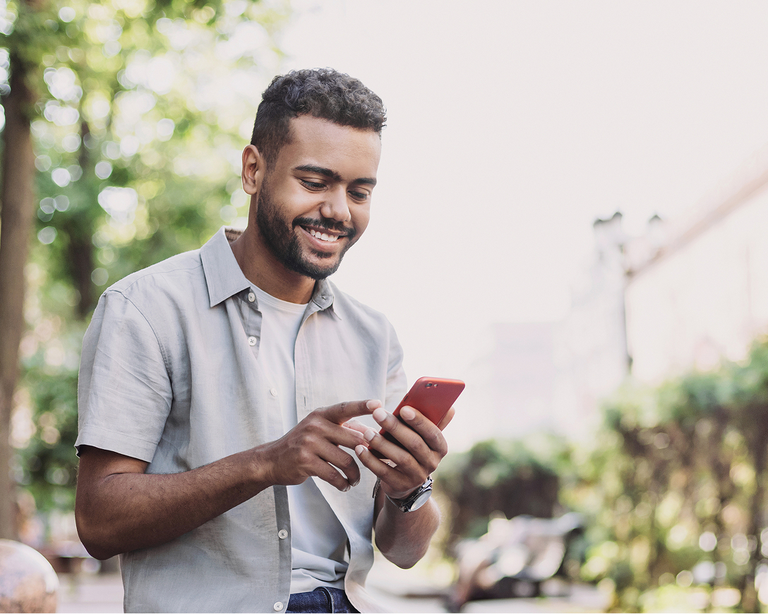 Man outside smiling while using his phone