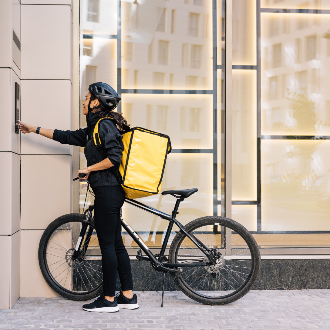 Deliver person with backpack and bicycle pressing a doorbell on a building