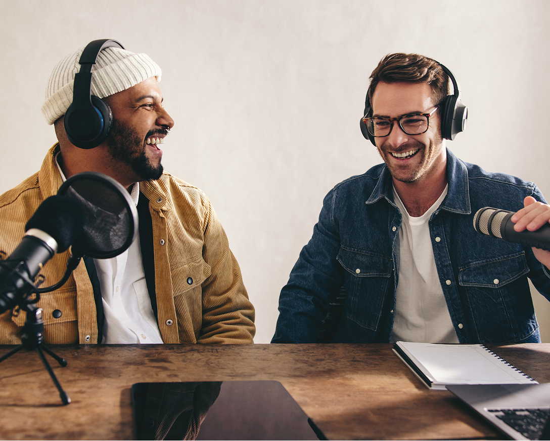 Two guys with headphones smiling and using microphones 