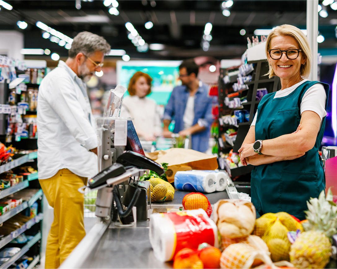 A cashier smiles as a man puts his groceries on the conveyer belt at the checkout counter